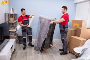 professional movers doing home relocation two young male wrapping sofa plastic wrap living room 210624645